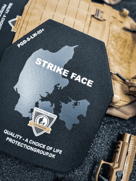 Kemény ballisztikai lap STRIKE FACE (PGD) oldallal; a háttérben plate carrier és szolgálati pisztoly, részlet a hordozóba helyezés előtt.