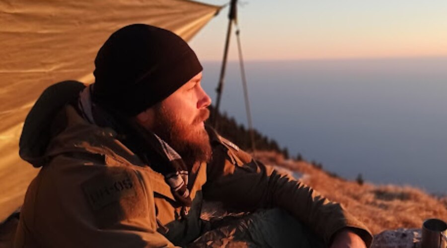 Egy férfi ül a naplementénél, és Snugpak márkájú Contact Fleece Beanie téli sapkát visel.
