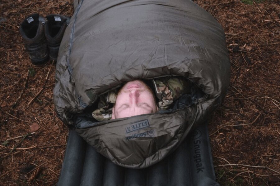 Egy terepszínű ruhás férfi felfújható matracon fekszik a Softie<sup>®</sup> Elite 5 Snugpak<sup>®</sup> hálózsákban. Forrás: Rigad, Snugpak