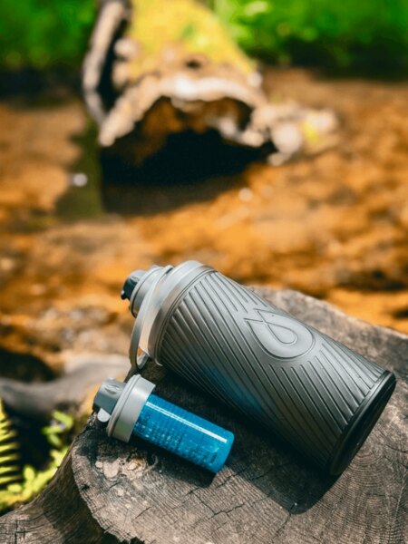 Flux HydraPak kulacs szűrős kupakkal egy tuskón a természetben, ideális utazáshoz és outdoor tevékenységekhez. Fotó: Rigad