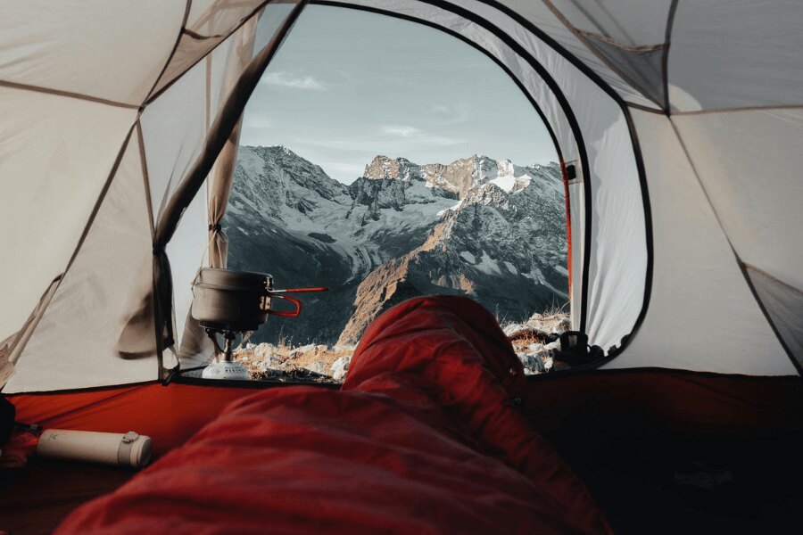 Kilátás a piros hálózsákból a havas hegyekre. Forrás: https://www.pexels.com/cs-cz/foto/krajina-hory-cestovani-dobrodruzstvi-9166687/