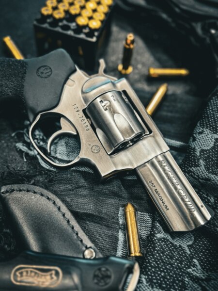 Ruger GP100 revolver .357 Magnum kaliberben, patronok és lövészkabát mellett elhelyezve.