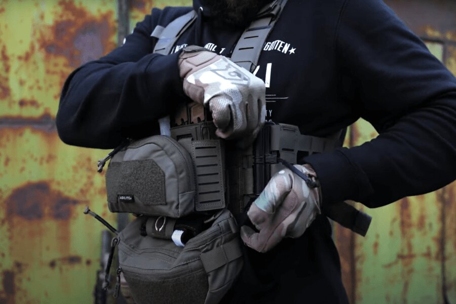 A férfi a Chest Rig Reaper™ Agilite Gear<sup>®</sup> felszereléssel és táskák segítségével állítja be a beállításokat. Forrás: Rigad - videó
