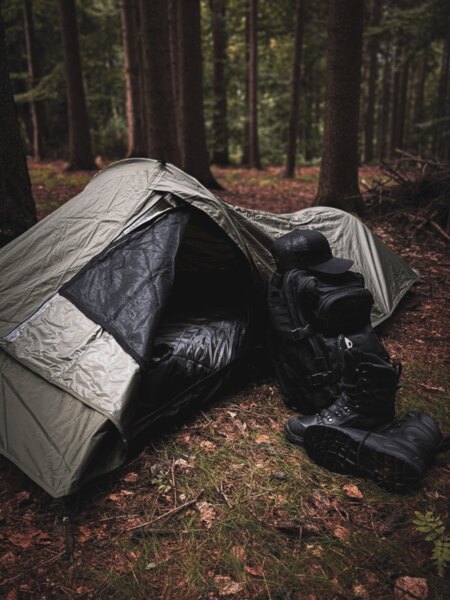 Snugpak bivakzsák kiterített hálózsákkal, mellette hátizsák és téli cipő, készen állva a sürgősségi éjszakázáshoz a természetben. Foto: Rigad