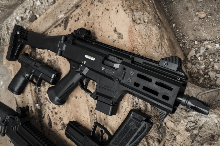 Modern CZ Skorpion EVO 3 géppisztoly kollimátorral és teleszkópos puskatussal a földön, a pisztolyok és tárak mellett. Foto: Rigad