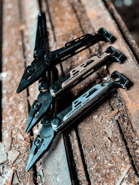 Három különböző színű Leatherman Signal multitool fa felületen.