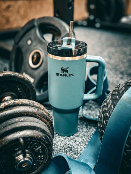 Stanley termoszívószálas bögre súlyzók és fitneszfelszerelés között elhelyezve.