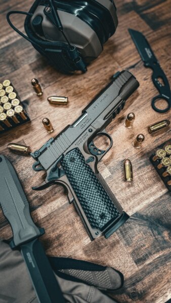 Schmeisser HUGO 1911 5" pisztoly .45 ACP kaliberben az asztalon lőszerrel és lőfegyver-kiegészítőkkel.