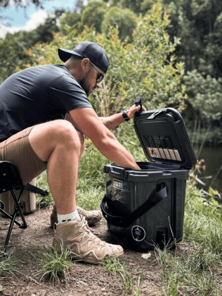 Egy férfi kinyitja a YETI LoadOut GoBox szállítódobozt, amikor víz közelében tartózkodik.