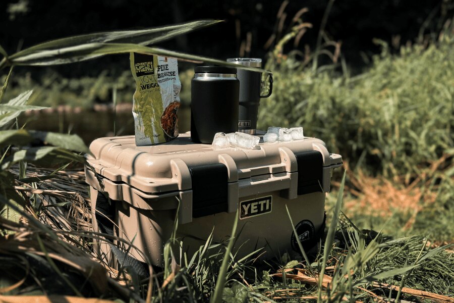 A YETI LoadOut GoBox szállítódoboz csomagolt étellel és termoszpoharakkal a természetben.