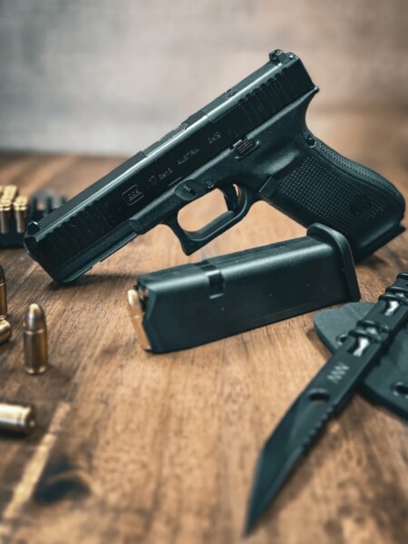 Asztalon Glock 17 Gen5 pisztoly mechanikus irányzékkal, tárral, lőszerrel és késsel.