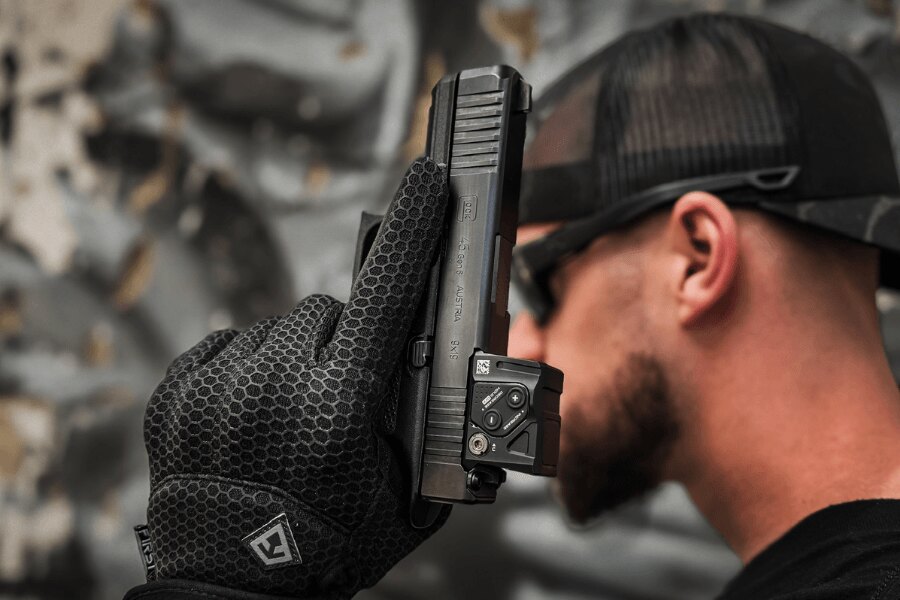 Részletesen egy Glock 45 pisztoly kolimátorral, kesztyűben tartva.