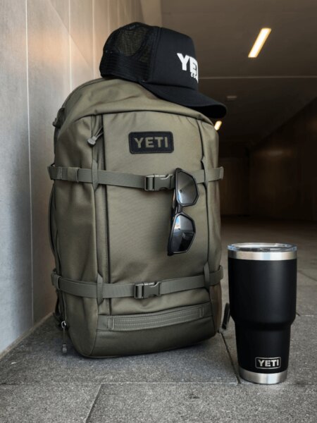 Világosszürke YETI Ranchero 27 l-es hátizsák sapkával és fekete YETI Rambler palackkal.