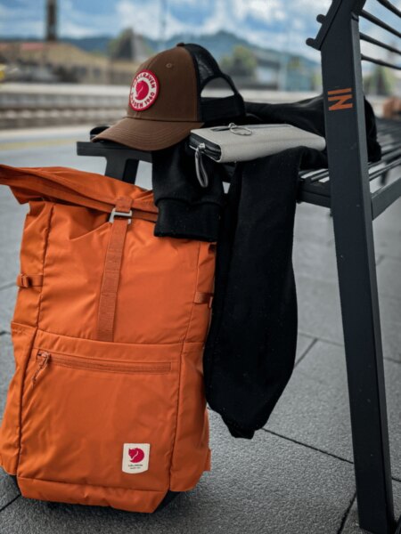 Fjällräven High Coast Foldsack 24 narancssárga hátizsák egy padhoz támasztva.